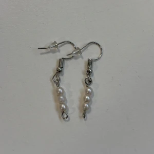 Örhängen med vita pärlor - Eleganta örhängen med vita pärlor på en silverfärgad krok. Perfekta för att ge en stilren touch till din outfit. Lätta och bekväma att bära hela dagen. Handgjorda av oss på Dahlia UF🌸