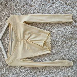 ribbad topp från Monki - Säljer en  ribbad topp från Monki i storlek XS. Toppen har långärmade ärmar och en v-ringad design med fina volangdetaljer vid nederkanten. 