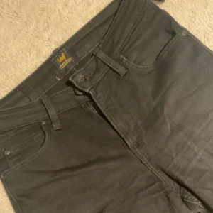Svarta jeans från Lee - Snygga svarta jeans från Lee med klassisk femficksdesign. De har en knapp och dragkedja framtill samt bälteshällor. defekt finns på sista bilden 