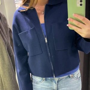 Mörkblå croppad cardigan med dragkedja - Snygg mörkblå croppad Cardigan med dragkedja framtill och två stora fickor. Från Åhléns. Modellen syns bättre på andra bilden. Säljer då jag har två likadana