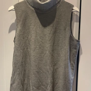 Grå ärmlös polotröja - Snygg grå ärmlös polotröja med ribbad krage. Perfekt för lager-på-lager eller som den är under varmare dagar. Enkel och stilren design som passar till det mesta.