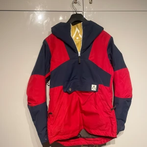 Röd och marinblå jacka från Wearcolour - Snygg och funktionell jacka från Wearcolour i rött och marinblått. Jackan har en dragkedja framtill och en praktisk huva. Perfekt för utomhusaktiviteter med sin sportiga design och slitstarka material. Används 1 gång då jag trillade och bröt mitt ben så den blev för liten 