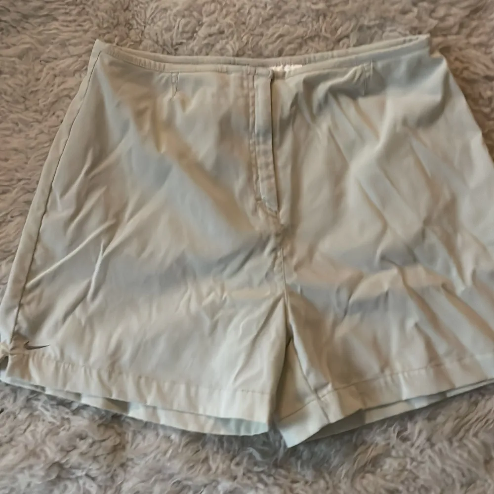 Säljer ett par stilrena beige shorts från Nike. De är i bra skick och har en enkel design med en liten slits på sidan. Perfekta för sommardagar eller träning. De har en normal passform och är tillverkade i ett lätt och bekvämt material.. Shorts.