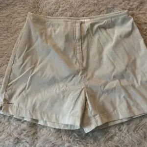 Säljer ett par stilrena beige shorts från Nike. De är i bra skick och har en enkel design med en liten slits på sidan. Perfekta för sommardagar eller träning. De har en normal passform och är tillverkade i ett lätt och bekvämt material.