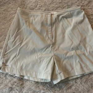 Beige shorts från Nike - Säljer ett par stilrena beige shorts från Nike. De är i bra skick och har en enkel design med en liten slits på sidan. Perfekta för sommardagar eller träning. De har en normal passform och är tillverkade i ett lätt och bekvämt material.