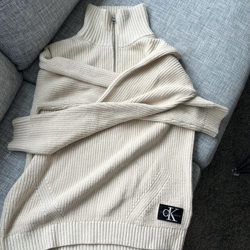 Säljer en superfin beige stickad tröja från Calvin Klein Jeans. Den har en halv dragkedja och långa ärmar, perfekt för kyliga dagar. Tröjan är i nyskick och har en snygg ribbad design. Passar perfekt till både vardag och lite finare tillfällen. 🧥✨.             Nypris ca 1200kr. Tröjor & Koftor.