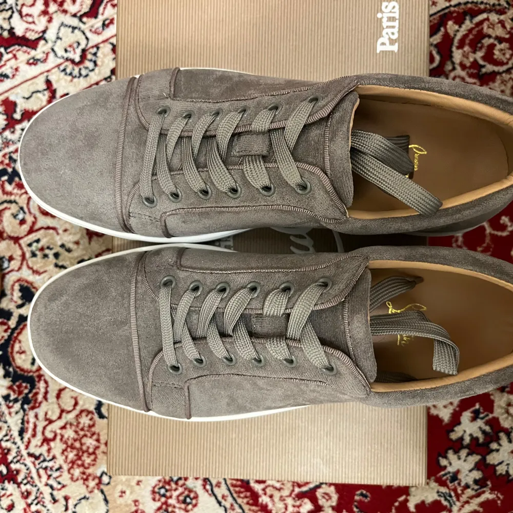 Säljer ett par snygga grå sneakers från Christian Louboutin i mocka. De har den ikoniska röda sulan och kommer med originalförpackning och äkthetsintyg. Perfekta för både vardag och fest! 🩶. Skor.