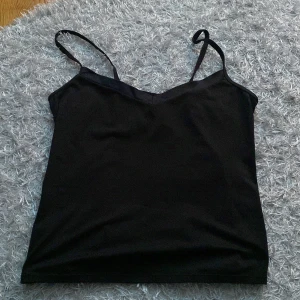 Svart ärmlös linnetopp - Säljer en stilren svart linnetopp i mycket bra skick. Den är ärmlös med smala axelband och har en enkel design som passar perfekt till både vardag och fest. Materialet känns mjukt och bekvämt mot huden.