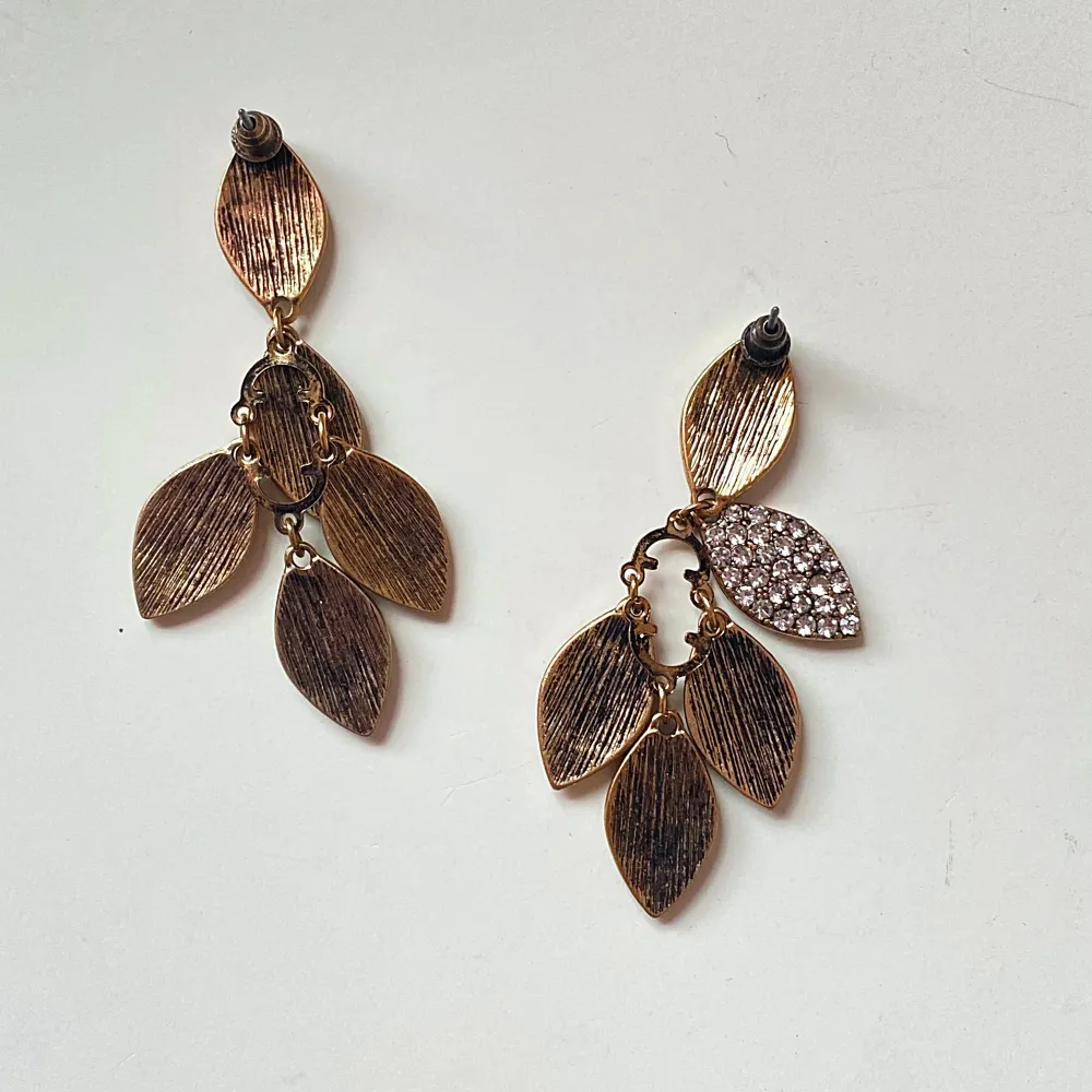 Säljer ett par superfina örhängen i bladform med massor av glittriga stenar. De är i en elegant guldton och mäter cirka 7 cm i längd. Perfekta för att lysa upp vilken fest som helst! ✨. Asusteet.