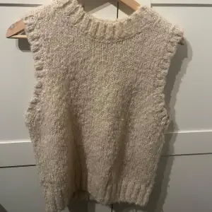 Mysig beige stickad väst från & Other Stories, perfekt för lager på lager under höst och vinter. Den har en ribbad kant vid hals och ärmar som ger en fin detalj.  Perfekt för en avslappnad men stilren look.