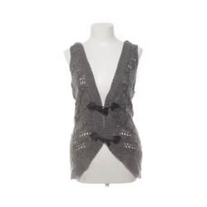 Grå stickad väst med huva - Säljer en snygg o unik grå stickad väst med huva. Den har ett öppet mönster och stängs med två knappar framtill. Perfekt för lager-på-lager under hösten eller våren. Västen är i normal passform och ger en avslappnad look.