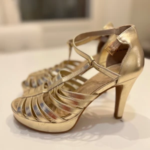 Ljust guldiga klackar 38 - Superbekväma och snygga med liten platå från märket Vox. Klackhöjd ca 10 cm. Mjuk sula. Perfekt för festliga tillfällen och som dansskor. Storlek 38. Innermått ca 24 cm, se bild.