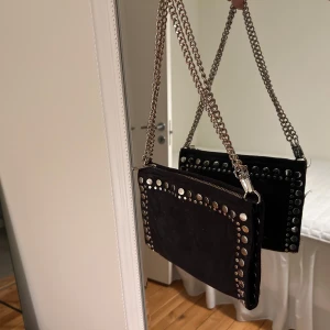 Svart axelväska med nitar - Snygg svart axelväska från zara. Säljs inte längre. Väskan har en kedja som kan användas både lång och kort! Perfekt för en kväll ute💞Lite sliten, därav priset!
