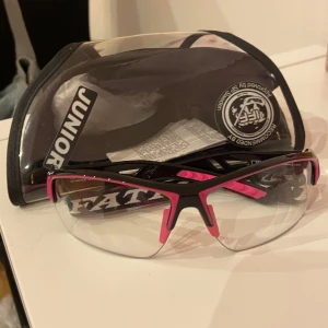 Svart och rosa Innebandy skyddsglasögon för juniorer - Säljer ett par coola innebandyglasögon från Fatpipe i juniorstorlek. De har en svart och rosa design med klara linser. Glasögonen kommer med ett skyddande fodral som har en tydlig 'Junior'-märkning. Den är knappt använd och har inga repor, superfint skick. 