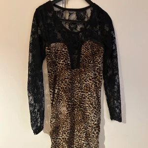 Leopardmönstrad klänning med spetsdetaljer - Snygg leopardmönstrad klänning med svarta spetsärmar och övre del. Klänningen har en tight passform och är tillverkad i ett mjukt material som formar sig efter kroppen. Den kommer inte till användning för mig längre. Kontakta mig för fler bilder eller info. 💕