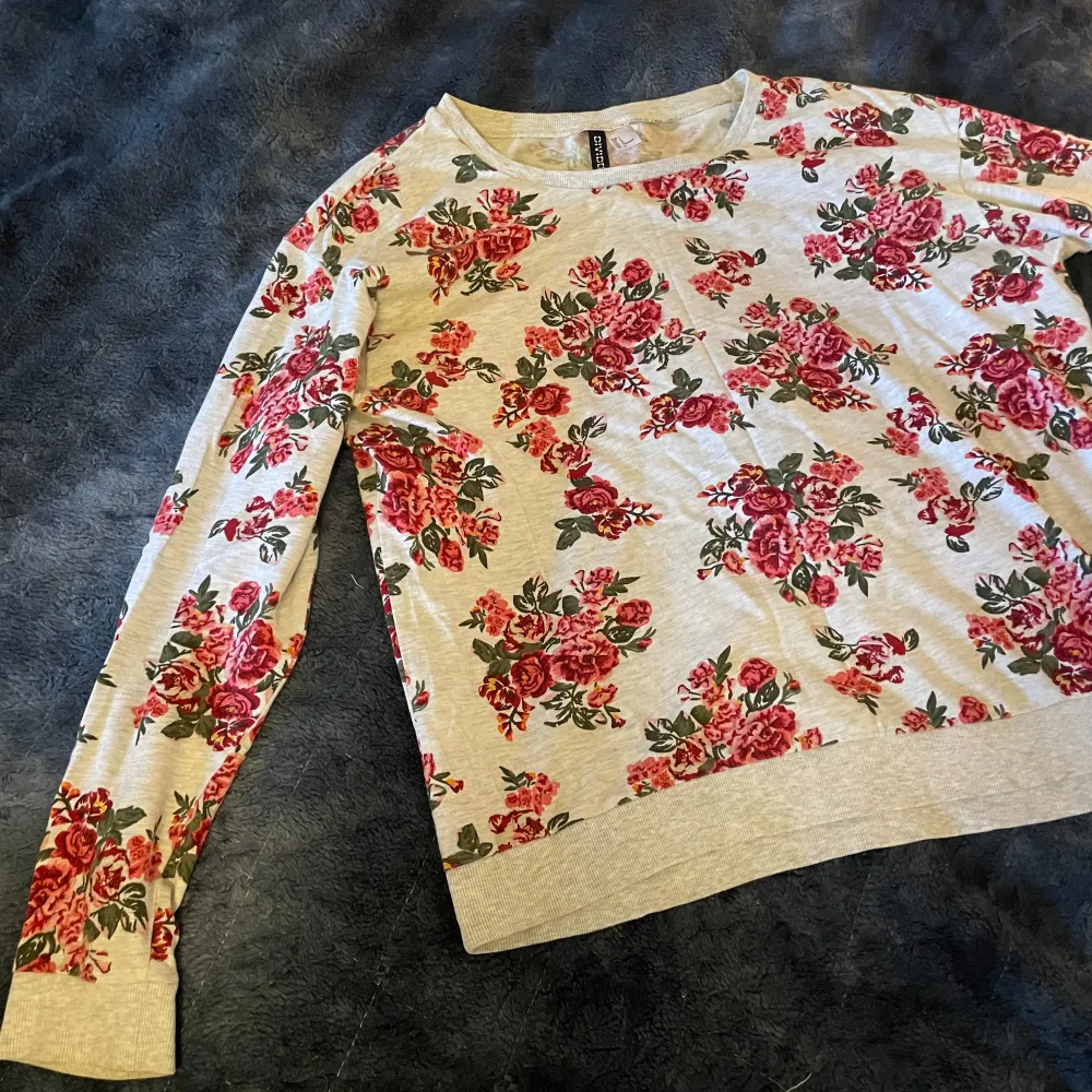 Säljer en superfin blommig tröja från H&M i storlek L. Den är beige med ett härligt mönster av röda rosor och gröna blad. Tröjan har långa ärmar och är perfekt för både vår och höst. Den är i bra skick och redo för nya äventyr! 🌸. Tröjor & Koftor.