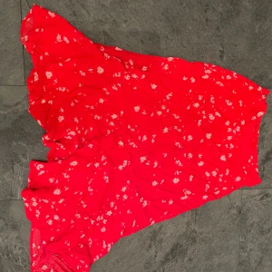 Röd blommig kjol - Superfin röd kjol med små rosa blommor, perfekt för sommardagar. Kjolen är längre i bak och har en dragkedja på sidan