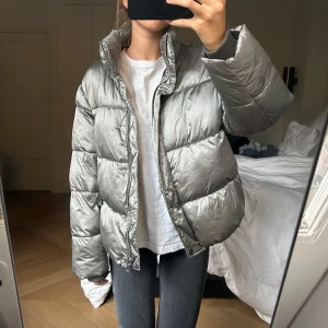 Vinterjacka  - Säljer denna puffer vinterjacka i en grön glansig färg. Kan stängas med både blixtlås och knappar. Bra skick! Trots att det står storlek 42 så är det så här den sitter på mig som är en S, den passar alltså många storlekar!