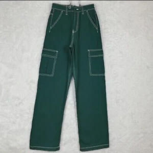 Gröna cargopants med vita sömmar - Säljer ett par gröna cargopants med kontrasterande vita sömmar. Byxorna har hög midja och stora fickor på sidorna, vilket ger en cool och praktisk look. Perfekta för en avslappnad stil eller en dag ute i naturen. De är i bra skick och redo för nya äventyr!