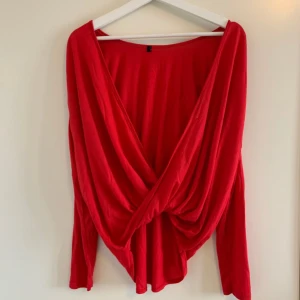 Röd omlottopp - Säljer en snygg röd omlottopp med långa ärmar. Perfekt för både vardag och fest! Toppen har en lös passform och är superbekväm att bära. Den djupa omlottdesignen ger en stilren look.