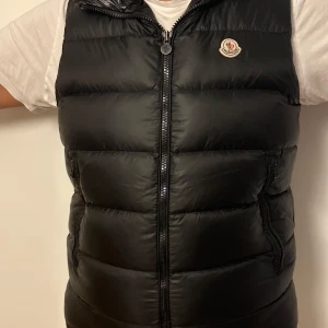 Moncler Down Montreuil Väst - Säljer min mans äkta Moncler Väst och är i gott skick. Medföljer kvitto och den har inga defekter. Vill bli av med den då jag är trött på att se den. NFC-kod finns i västen.Den har en huva med Moncler-logga i stora bokstäver. Perfekt för höst och vin