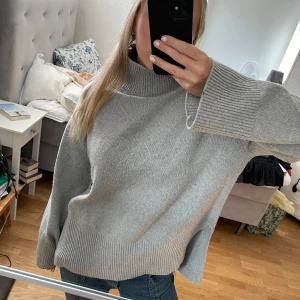 Grå stickad tröja - Säljer en supermysig grå stickad tröja med hög krage. Den har långa ärmar och en lös passform som gör den perfekt för kyliga dagar. Tröjan är i bra skick och passar perfekt till jeans för en avslappnad look.😍😍 Den är lite nopprig därav priset