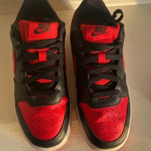 Nike Air Jordans i svart och rött - Säljer ett par snygga Nike Air Jordans i svart och rött. Nya kostar 750kr! Skorna har en klassisk design med svart läder och röda detaljer. De har en röd sula och svart snörning. Det finns några små fläckar på sulan men det går enkelt bort!
