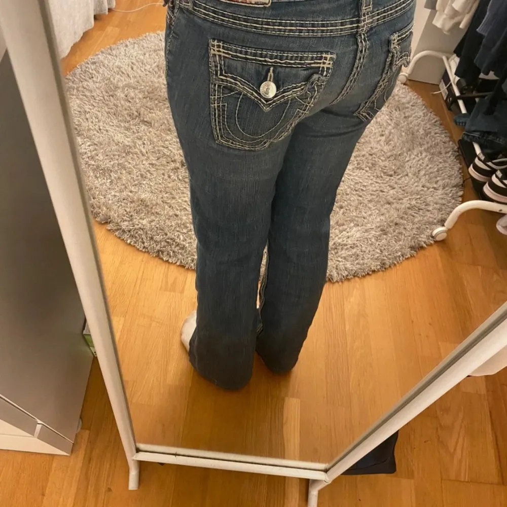 Säljer ett par snygga blå jeans från True Religion. De har en bootcut passform och är i en klassisk blå färg med snygga sömmar och detaljer på bakfickorna. Perfekta för en casual look eller att klä upp med en snygg topp. De är i bra skick och redo fö. Jeans & Byxor.