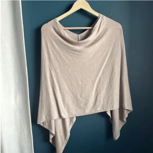 Beige Poncho  - En snygg och bekväm poncho i en ljus beige färg. Den har en enkel design med en v-ringning bak och en lös passform.