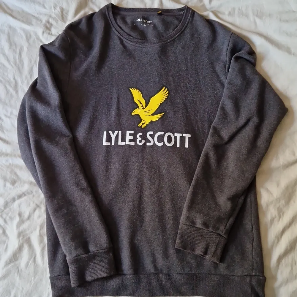 Säljer en snygg grå tröja från Lyle & Scott i storlek L. Den är gjord av 100% bomull och har ett stort gult örnmärke på bröstet. Perfekt för en avslappnad stil och passar bra till både jeans och chinos. Tröjan är i bra skick och snygg att ha på sig.. Tröjor & Koftor.