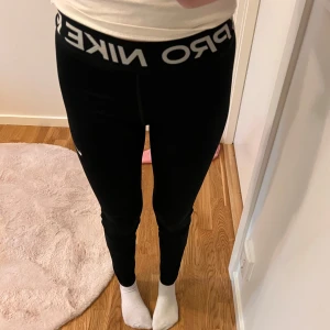 Svarta leggings från Nike - Säljer ett par svarta leggings från Nike. De är superbekväma och perfekta för träning eller bara att chilla i. De har en elastisk midja med Nike-loggan i vitt. Passar perfekt för dig som gillar en tight passform.