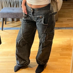 Baggy jeans från Culture - Säljer ett par coola jeans från Culture i storlek 38. De är mörkblå och har en loose passform med snygga detaljer som knappar och snörning vid benslutet.