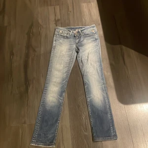 Blå jeans med dragkedjedetaljer - Säljer ett par snygga blå jeans med coola dragkedjedetaljer på bakfickorna. De har en klassisk femficksdesign och en lätt tvättad look som ger dem en avslappnad stil. Perfekta för vardagsbruk! Andvänd en gång 