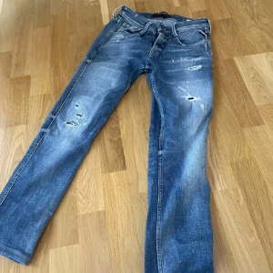 REPLAY JEANS MED SLITNINGAR - Säljer ett par blå jeans med slitningar på framsidan från replay. 10/10 aldrig använda De har en klassisk femficksdesign och en bekväm passform. Perfekta för en avslappnad stil!