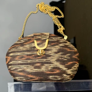 Unik Mönstrad kuvertväska med guldkedja - Axelremsväska med ett unikt mönster i bruna och orange toner. Väskan har en elegant lång guldkedja som axelrem. ”Hård” modell med något tyg på. Mått -se bild med linjal. Hämtas på Hägerstensåsen eller ök 🧡🤍🤎