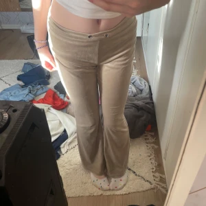Beige byxor från Gina Tricot - Säljer ett par snygga beige byxor från Gina Tricot i storlek XS. De är i ett mjukt och bekvämt material, perfekt för en avslappnad stil. Byxorna har en låg midja och en bootcut-stil som ger en retro känsla. De har också dekorativa knappar framtill och en praktisk bakficka.