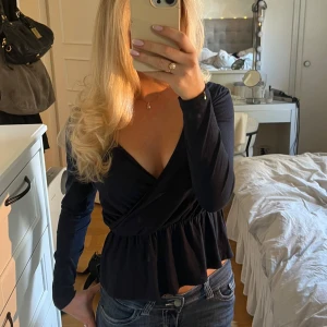 Mörkblå omlott topp - En jättefin marinblå/mörkblå topp. Designen är omlott och man kan välja lite själv hur djupt man vill att v-ritningen ska gå. TIPS!!! Om man inte vill ha så v-ringat och att den ska hålla sig på plats så kan man sätta dit ett örhänge🥰(se sista bild)