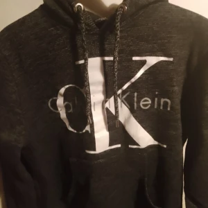 Svart hoodie från Calvin Klein - Säljer en snygg och bekväm svart hoodie från Calvin Klein. Den har en stor logga på framsidan och justerbara snören i huvan. Passar till alla tillfällen!