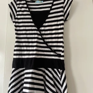 Randig klänning från Fish Bowl - Säljer en superfin randig klänning från Fish Bowl. Den har ett coolt svart och vitt randigt mönster och en snygg omlott-design framtill. Klänningen är kortärmad och perfekt för både vardag och fest. Den är gjord i ett mjukt och bekvämt material som känns skönt mot huden.