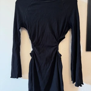 Svart klänning - Svart långärmad klänning med hål på sidorna, ej använd