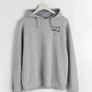 Grå hoodie  - Säljer en supermjuk och bekväm grå hoodie med texten ’JE M’EN AMOUR’ och en stjärna tryck på både framsidan och baksidan. Har bara använts ett få tals gånger. Jag säljer den för att jag inte använder den längre köpte den för 249kr