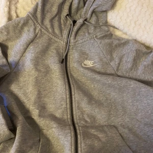 Grå hoodie från Nike - Säljer en klassisk grå hoodie från Nike i storlek S. Den har en dragkedja framtill och en justerbar huva med snören. Perfekt för en avslappnad stil eller träning. Superbekväm och lätt att matcha med allt!