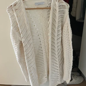 Vit stickad kofta från Twinset - Säljer en superfin vit stickad kofta från Twinset, tillverkad i Italien. Den är gjord av 90% bomull och 10% polyester, vilket gör den både mjuk och hållbar. Perfekt för att hålla sig varm under kyliga vår- och höstdagar. Koftan har ett öppet mönster som ger en luftig känsla och är perfekt att slänga över en topp eller klänning.