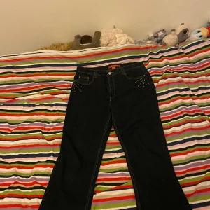 Svarta jeans med broderade detaljer - Säljer ett par snygga svarta jeans från Cos Jeans. De har coola broderade detaljer på bakfickorna och små nitar fram. Jeansen är i storlek 12 och är gjorda av en blandning av ramie, bomull, polyester och spandex för en skön passform.