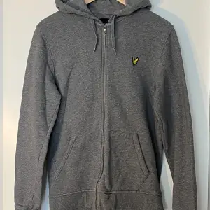 Säljer en snygg och bekväm grå hoodie från Lyle & Scott. Den har en dragkedja framtill och en liten broderad logga på bröstet. Perfekt för året om.