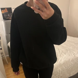 Svart sweatshirt med Brooklyn-tryck - Säljer en svart sweatshirt med tryck på baksidan som säger 'BROOKLYN 1898 Memories of New York side'. Den är superbekväm och perfekt för en casual look. Tröjan har långa ärmar och en normal passform. Perfekt för höst och vinter!