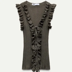 Khaki ribbad topp från Zara - Säljer en superfin brun ribbad topp från Zara. Den har volangdetaljer längs ärmarna och en snygg knytning framtill. Perfekt för både vardag och fest! Toppen är ärmlös och har en v-ringad design som ger en elegant touch.