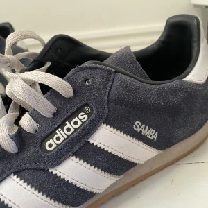 Adidas Samba i mocka - Säljer ett par klassiska Adidas Samba i mörkblå mocka med vita detaljer. Skorna har en snygg retrostil och är bra för både vardag och fest! 🕺Lägg gärna ett bud!