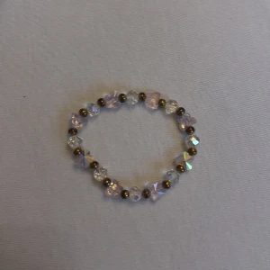 Glittrigt armband med pärlor - Säljer ett superfint armband med glittriga pärlor i olika färger. Pärlorna är genomskinliga med en regnbågsskimrande effekt och små guldiga pärlor emellan. Perfekt för att ge lite extra bling till din outfit! Passar bra till både vardag och fest.