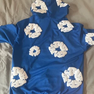 Denim tears hoodie  - Säljer en cool blå hoodie med unika vita molnmönster. Perfekt för att sticka ut i mängden! Den har en bekväm passform och en praktisk huva. Materialet känns mjukt och skönt mot huden. Perfekt för både vardag och chill dagar. 🌀